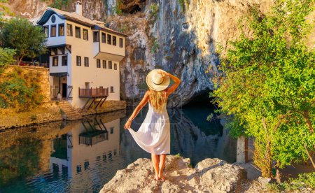 Foto de Mujer turista en vestido blanco disfrutar de la vista del monasterio, el río y la cueva en el pueblo de Blagj, el río Buna turismo turístico, destino de viaje, vacaciones en Bosnia - Imagen libre de derechos