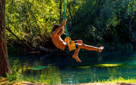 Téléchargez les photos : Jeune garçon s'amuser sur swing sur arbre au-dessus d'un lac - en image libre de droit