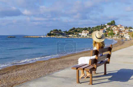 Foto de Destino turístico Grecia- mujer turista sentada en el banco disfrutando de la calma y la vista del mar y el pueblo - Imagen libre de derechos