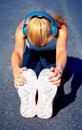 Foto de Mujer estirando sus piernas en el suelo antes de trotar, entrenamiento cardiovascular o entrenamiento - Imagen libre de derechos