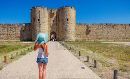 Téléchargez les photos : Murs de ville célèbres français- Aigues Mortes- Touriste WOman avec chapeau bleu profitant mur environnant - en image libre de droit