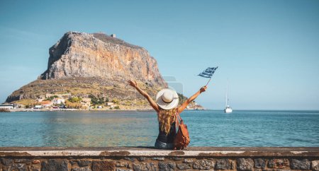 Foto de Mujer feliz turista con bolsa y bandera disfrutando de vacaciones en Grecia Monemvasia isla - Imagen libre de derechos