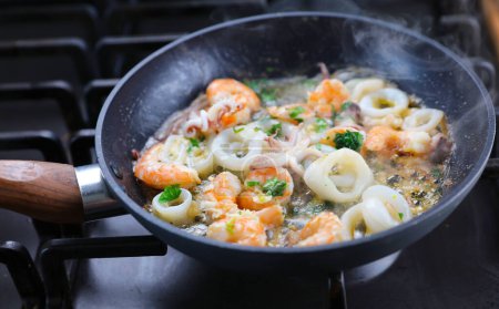 Téléchargez les photos : Crevettes à l'ail et poulpe à la sauce beurre et persil - Faire frire les fruits de mer dans une poêle à wok - en image libre de droit