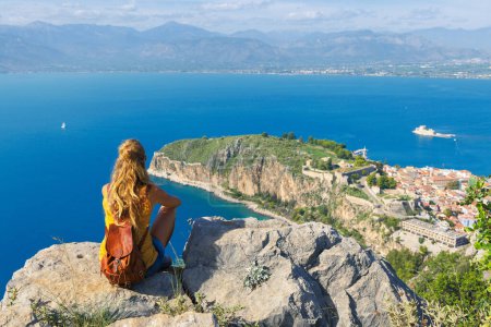 Foto de Vista trasera de la mujer turista sentado y mirando a la ciudad de Nafplio desde el castillo de Palamidi en el Peloponeso. Países Bajos - Imagen libre de derechos