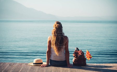Foto de Vista trasera de la mujer sentada en el muelle de madera admirando el lago Ohrid en Macedonia-viajes, vacaciones, aventura, concepto relajante - Imagen libre de derechos
