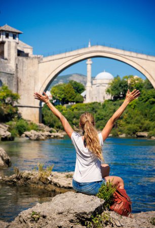 Téléchargez les photos : Touriste féminine regardant le célèbre vieux pont et la rivière de Mostar- tourisme d'excursion, Voyage, vacances en Bosnie - en image libre de droit