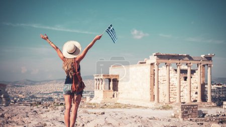 Foto de Mujer joven viajera con sombrero, bolso y bandera griega en Atenas, Acrópolis - Imagen libre de derechos