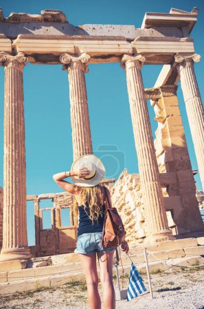 Photo for Caucasian traveler with hat, bag and greek flag looking at ruins, temple in Greece - Royalty Free Image