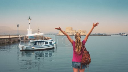 Photo for Traveler female enjoys The Bourtzi water castle and traditional fishing boat in Greece, Nafplio, Peloponnese - Royalty Free Image