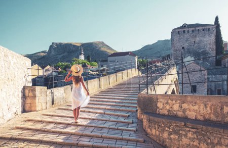Téléchargez les photos : Touriste féminine avec robe blanche sur le célèbre vieux pont de la ville de Mostar en Bosnie-Herzégovine - en image libre de droit