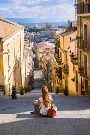 Téléchargez les photos : Femme touristique avec drapeau italien assis sur les escaliers et profitant du centre-ville de Caltagirone. Voyages, tourisme en Sicile île - en image libre de droit