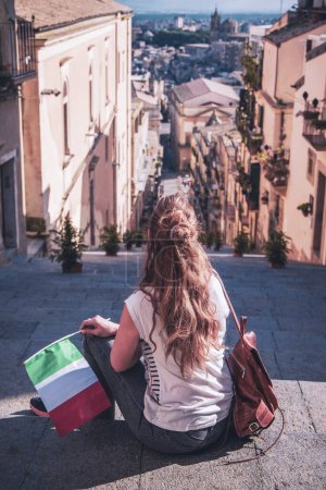 Foto de Turista con bandera italiana sentada en las escaleras y disfrutando del centro de la ciudad de Caltagirone. Viajar, el turismo en Sicilia isla - Imagen libre de derechos
