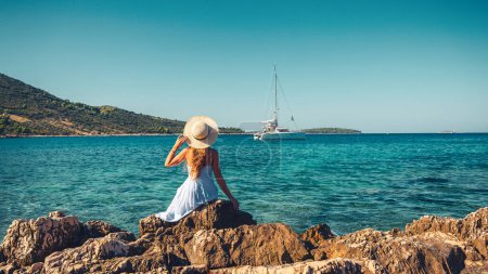 Téléchargez les photos : Une fille avec chapeau et robe blanche regardant yacht sur la mer - en image libre de droit
