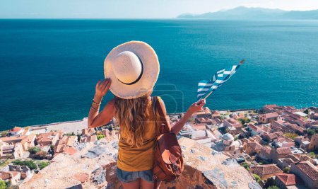 Photo for Travel destination in Greece-Traveler woman with bag, hat and Greek flag-Road trip, Adventure, summer vacation concept - Royalty Free Image