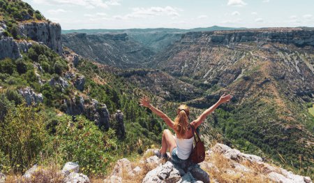 Téléchargez les photos : Femme heureuse assise sur le rocher bénéficiant d'une belle vue panoramique sur le paysage - en image libre de droit