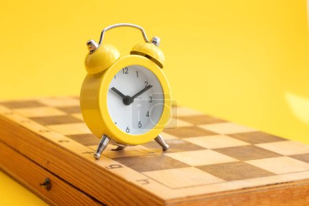 Foto de Yellow alarm clock on a chess board. - Imagen libre de derechos