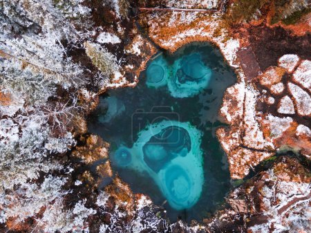 Blue geyser lake in autumn forest after snowfall. Altai mountains, Siberia, Russia. Aerial top down view. Autumn landscape