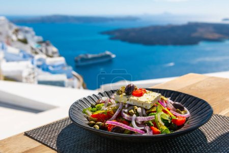 Téléchargez les photos : Salade grecque avec belle vue sur la mer dans l'île de Santorin, Grèce. Concept national de cuisine grecque. Voyages et vacances - en image libre de droit