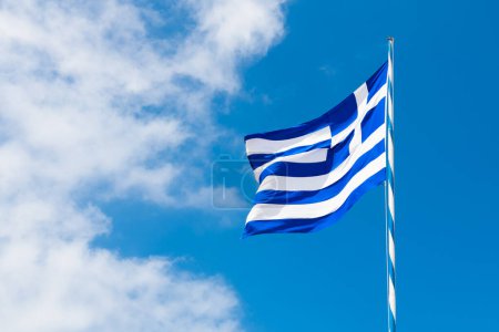 Drapeau de la Grèce contre le ciel bleu avec des nuages blancs. Drapeau agitant dans le vent léger dans la journée ensoleillée d'été