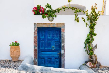 Weiße kykladische Architektur auf der Insel Santorin, Griechenland. Blaue Holztür mit Zierbaum und Blumen. 