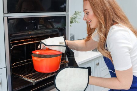 Foto de Young woman is preparing in the kitchen. Healthy Food. Salad. Diet. Dieting Concept. Healthy Lifestyle. Cooking At Home. Prepare Food. Taking the pot out of the oven in oven mitts - Imagen libre de derechos