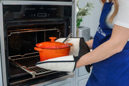 Téléchargez les photos : Young woman is preparing in the kitchen. Healthy Food. Salad. Diet. Dieting Concept. Healthy Lifestyle. Cooking At Home. Prepare Food. Taking the pot out of the oven in oven mitts - en image libre de droit