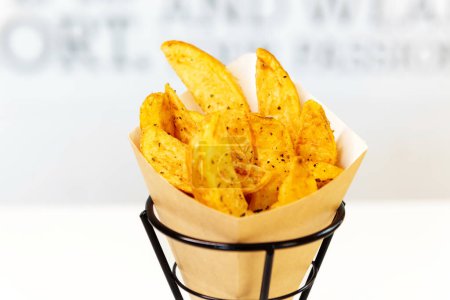 Téléchargez les photos : Oven baked potato wedges with sea salt and herbs. fries in a recyclable paper bag, popular fast street food - en image libre de droit