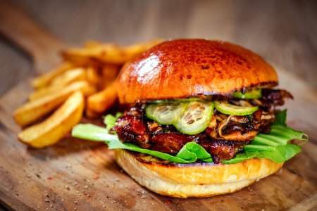 Téléchargez les photos : Burger avec côtes de porc, servi avec concombre et sauce teriyaki trempée sur une planche à découper en bois - en image libre de droit