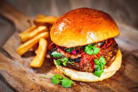 Téléchargez les photos : Burger juteux avec côtes de porc, sauce tomate, légumes frais et coriandre sur une planche à découper en bois - en image libre de droit