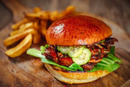 Téléchargez les photos : Burger avec côtes de porc, servi avec concombre et sauce teriyaki trempée sur une planche à découper en bois - en image libre de droit