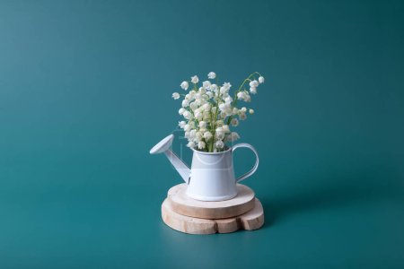 Lilies of the valley bouquet in a mini watering can on a turquoise background.