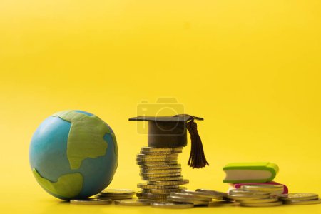 Photo for Graduated cap with coins and globe on yellow background. Savings for education concept. - Royalty Free Image