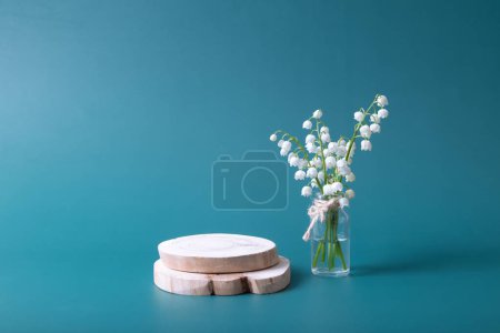Téléchargez les photos : Wooden podium or pedestal with lilies of the valley bouquet in a miniature glass jar on a turquoise background. - en image libre de droit