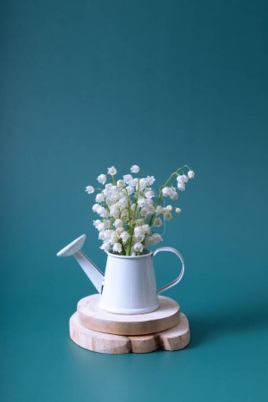 Lilies of the valley bouquet in a mini watering can on a turquoise background vertical format.