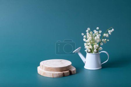 Wooden podium or pedestal with lilies of the valley bouquet in a watering can on a turquoise background.