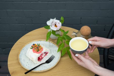 Téléchargez les photos : Une tasse de thé vert dans les mains et un rouleau de meringue sur la table du café. Nourriture sucrée Nature morte. - en image libre de droit