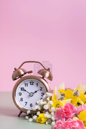 Foto de Reloj despertador con flores de primavera. Primavera, concepto de ahorro de luz, primavera hacia adelante. Copiar espacio - Imagen libre de derechos