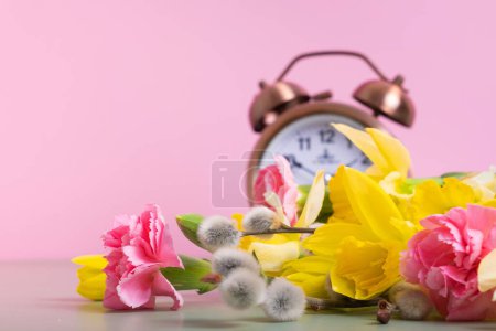 Foto de Flores de primavera con despertador desenfocado. Primavera, concepto de ahorro de luz natural, primavera hacia adelante. - Imagen libre de derechos