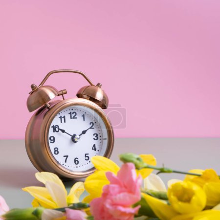 Foto de Reloj despertador con flores primaverales sobre fondo de color. Primavera, concepto de ahorro de luz, primavera hacia adelante. Copiar espacio - Imagen libre de derechos