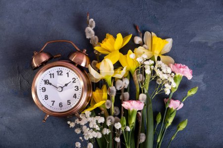 Foto de Reloj despertador con flores de primavera. Primavera, concepto de ahorro de luz natural, primavera hacia adelante. - Imagen libre de derechos