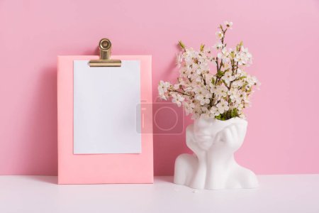 Foto de Papel de hoja vacía con jarrón en forma de cabeza con flores de primavera sobre fondo rosa. - Imagen libre de derechos