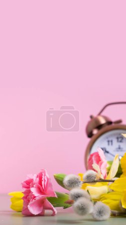 Foto de Flores de primavera con despertador desenfocado. Primavera, concepto de ahorro de luz, primavera hacia adelante. Copiar espacio - Imagen libre de derechos