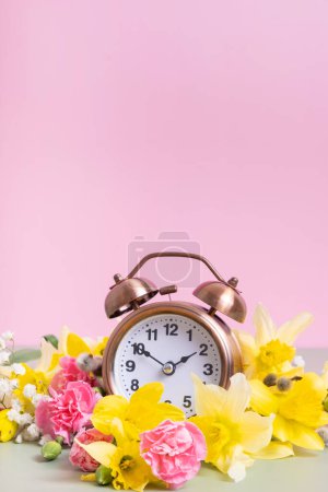 Foto de Reloj despertador con flores amarillas y rosadas. Primavera, concepto de ahorro de luz natural, primavera hacia adelante. - Imagen libre de derechos