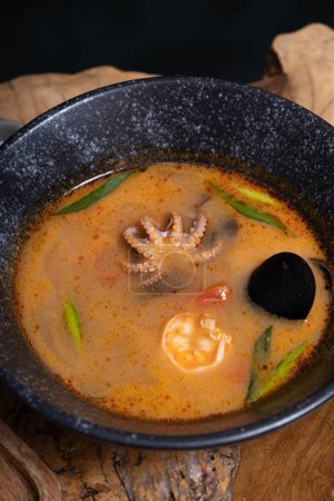 Tom yum soup with shrimps and Octopus on a wooden table angle view.