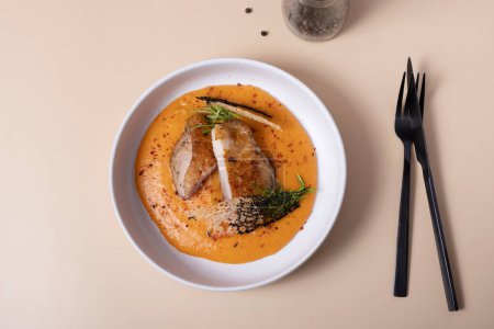 A plate with fried chicken and carrot and potato puree with black cutlery on beige background top view.