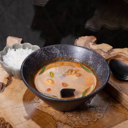 Tom yum soup with seafood and rice on wooden table angle view.