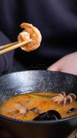 Shrimp on chopsticks on the background of tom yum soup.