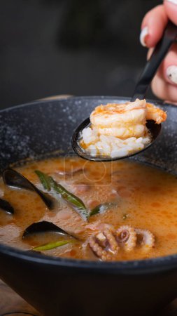 Shrimp and rice on spoon in woman's hand on the background of tom yum soup.
