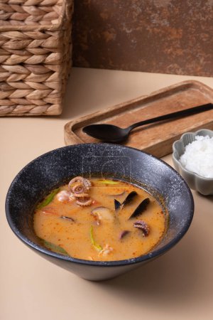 Tom yum soup with seafood and rice on beige background angle view.