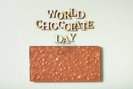 Text zum Weltschokoladentag mit Schokolade flach gelegt, Draufsicht auf pastellgrünem Hintergrund.